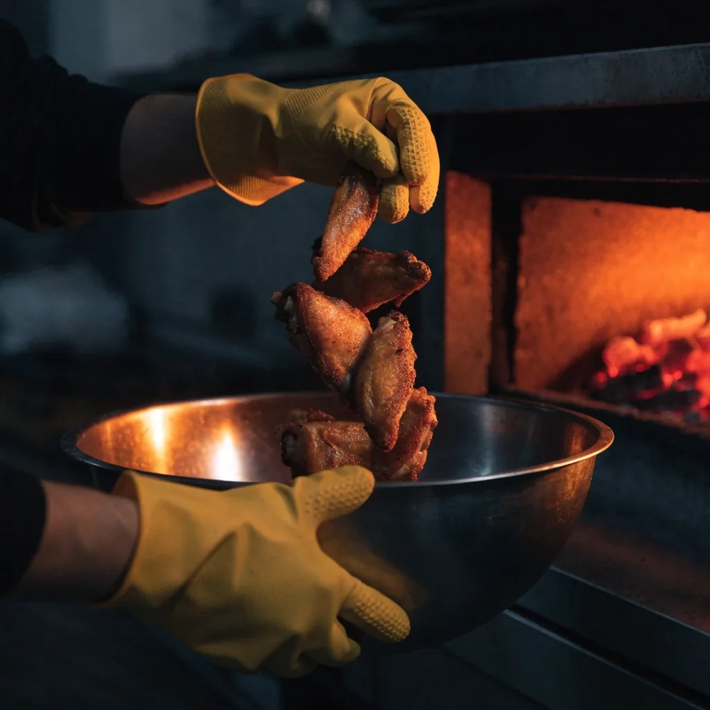Roasted chicken wings beside a glowing coal-fired oven